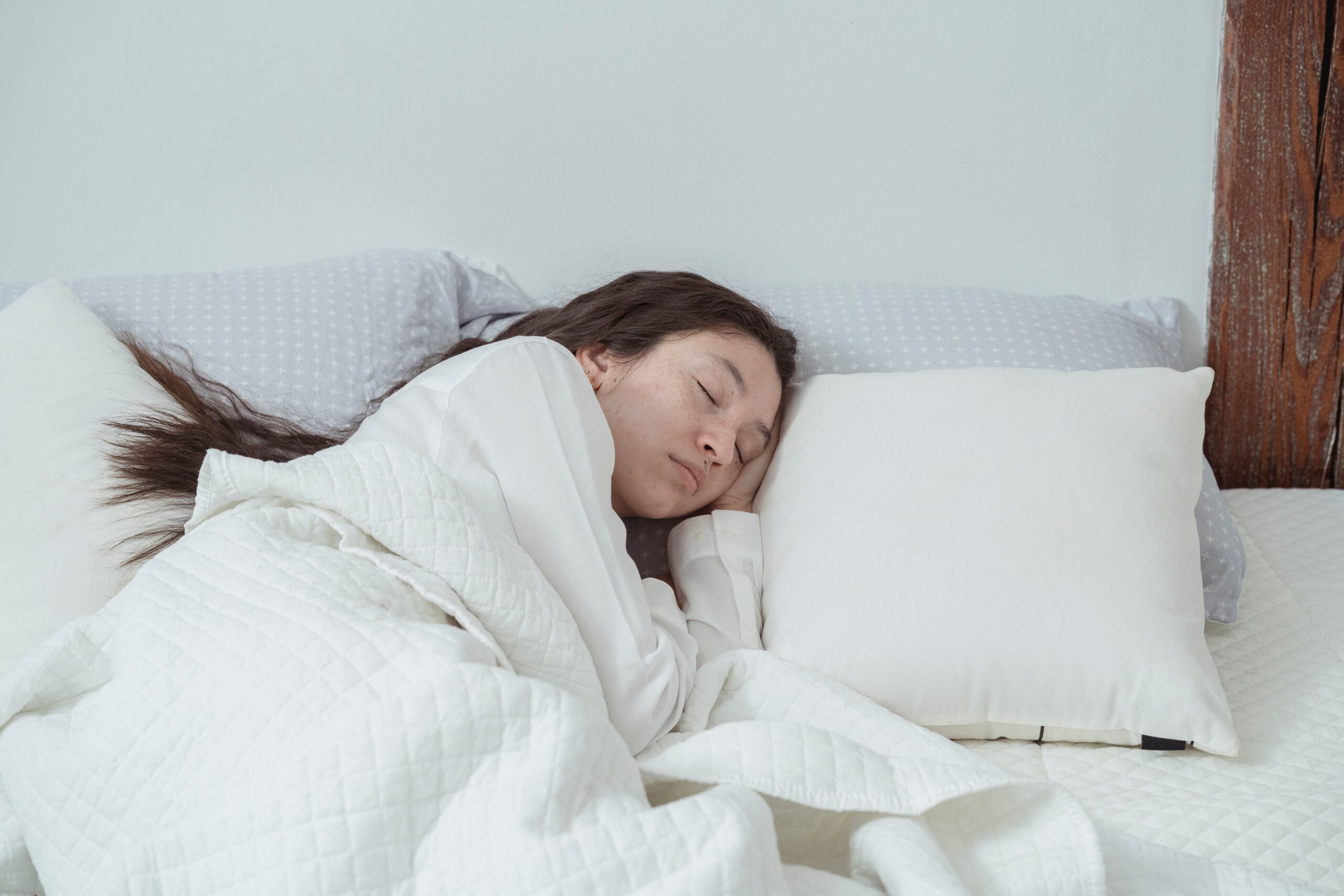 a woman sleeping serenely in bed, surrounded by white bedding and pillows.