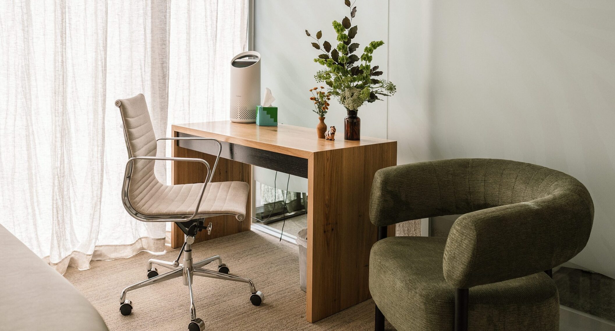 A desk, desk chair, and comfy chair forming the corner of a typical consultation room at Zebras. The room is light-filled, with sunlight streaming through a sheer curtain to the left. A leafy plant sits atop the desk.